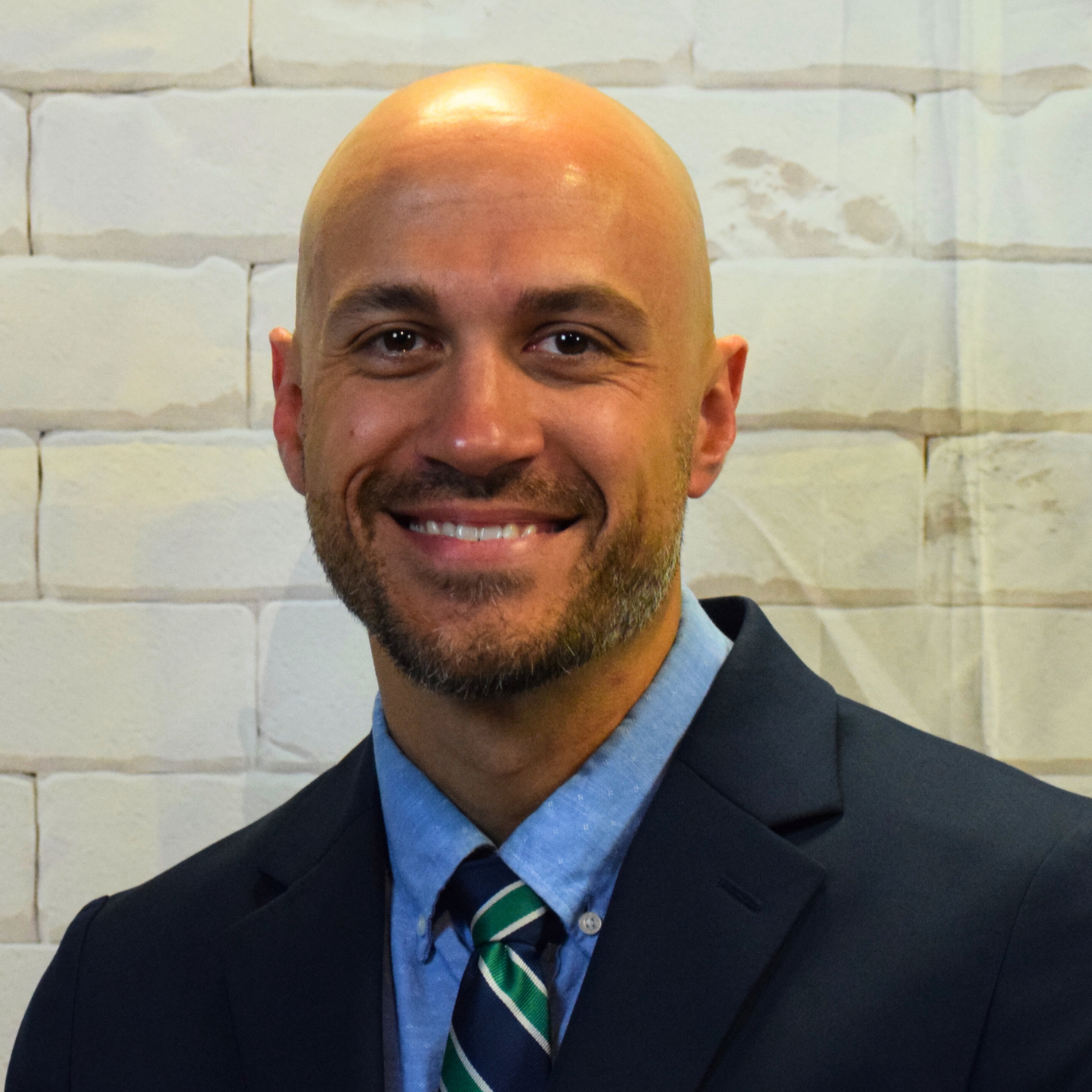  A bald man in a suit and tie smiles warmly, exuding confidence and professionalism.