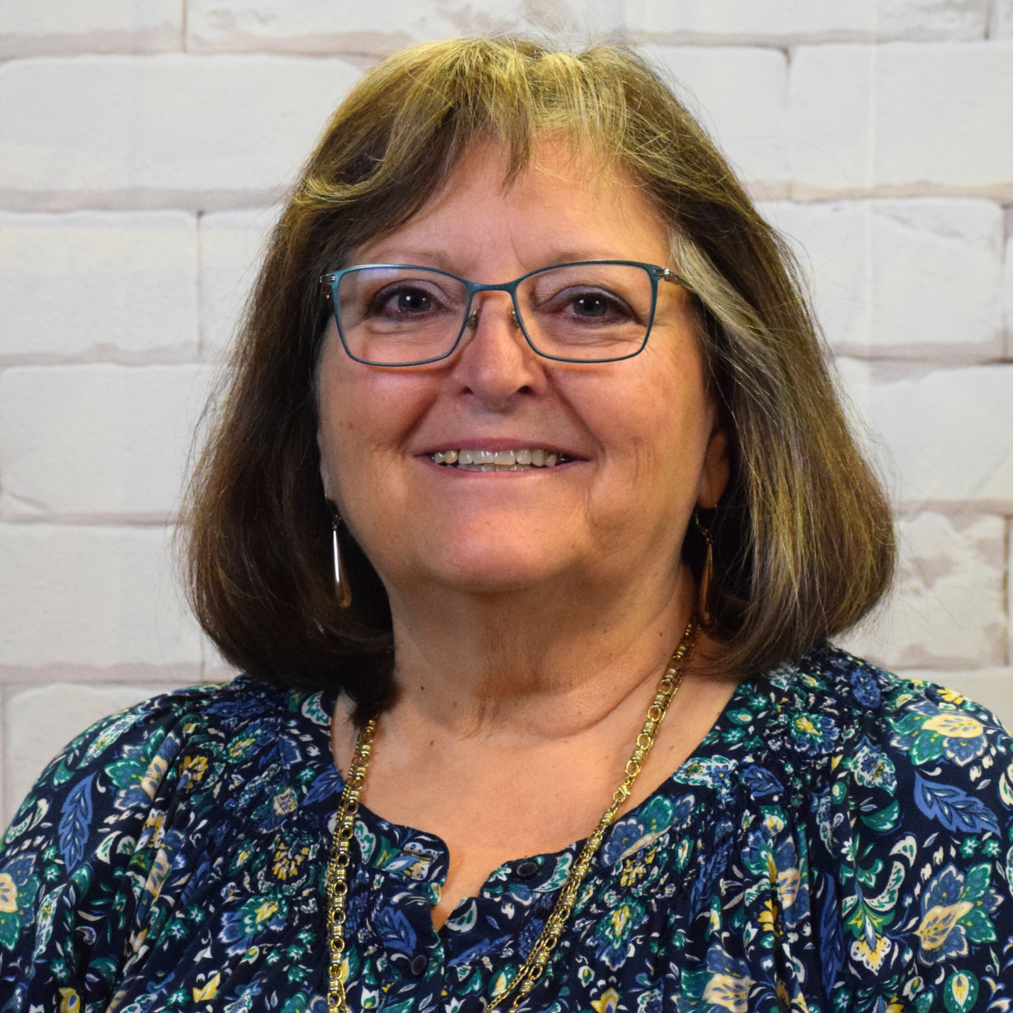  A woman wearing glasses and a blue shirt smiles warmly, exuding a friendly and approachable demeanor.