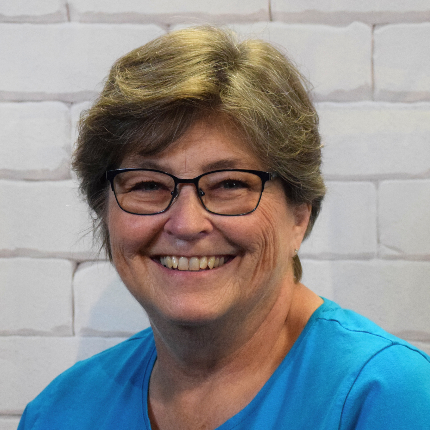 A woman wearing glasses and a red sweater smiles warmly, exuding a friendly and approachable demeanor.