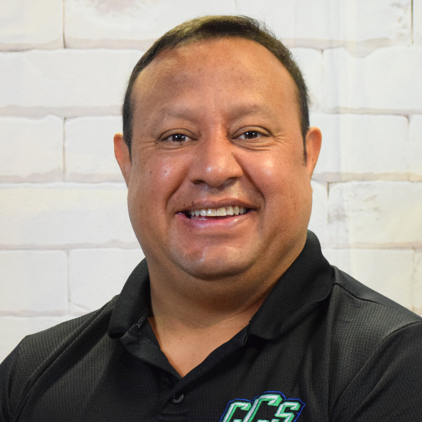 A man wearing a black shirt smiles warmly at the camera, exuding a friendly and approachable demeanor.
