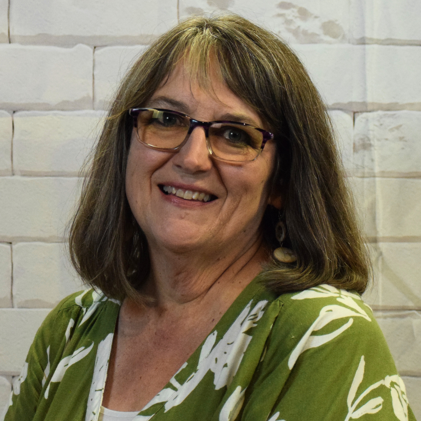 A woman with glasses wearing a polka dot shirt, smiling and looking confidently at the camera.