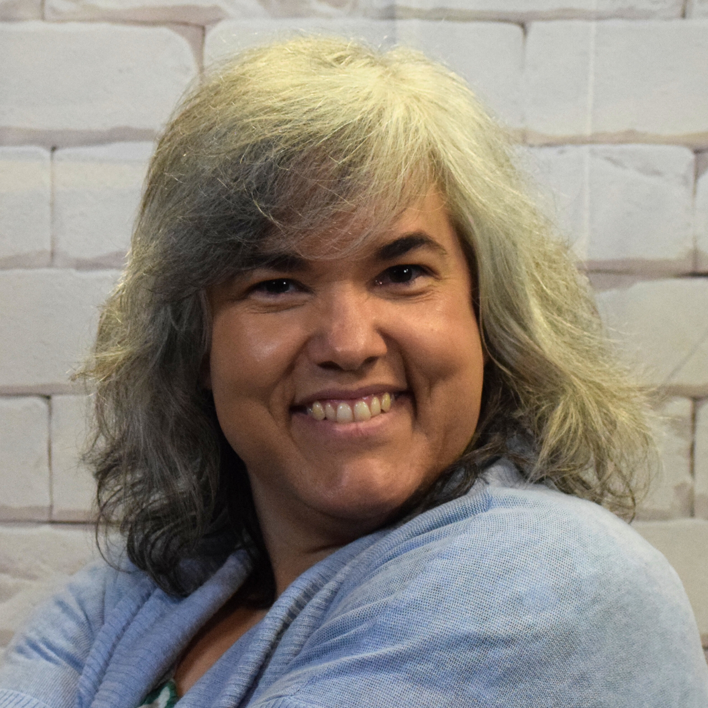 A woman with gray hair wearing a black and white shirt, smiling softly against a neutral background.