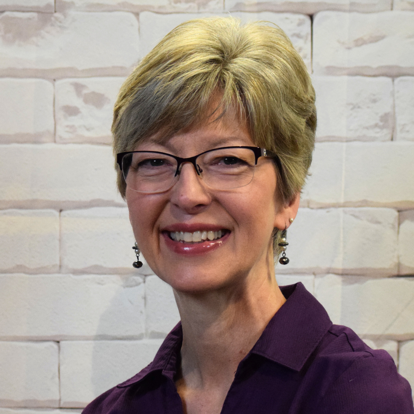  A woman wearing glasses and a black shirt smiles warmly, exuding confidence and approachability.