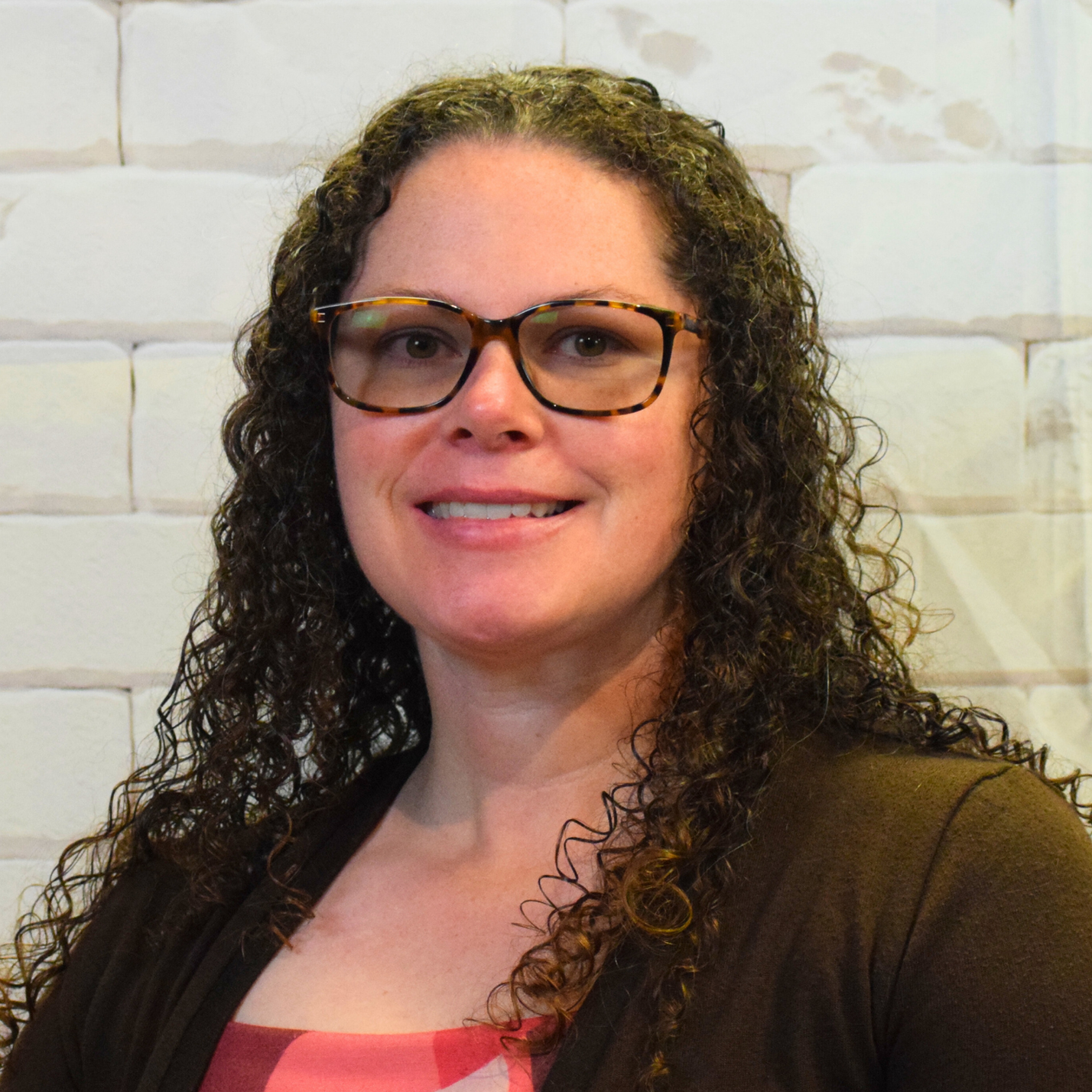  A woman with curly hair and glasses smiles warmly, exuding joy and confidence in her expression.