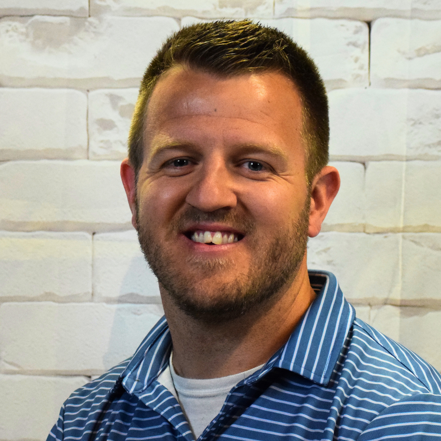 A man wearing a plaid shirt smiles warmly at the camera, exuding a friendly and approachable demeanor.