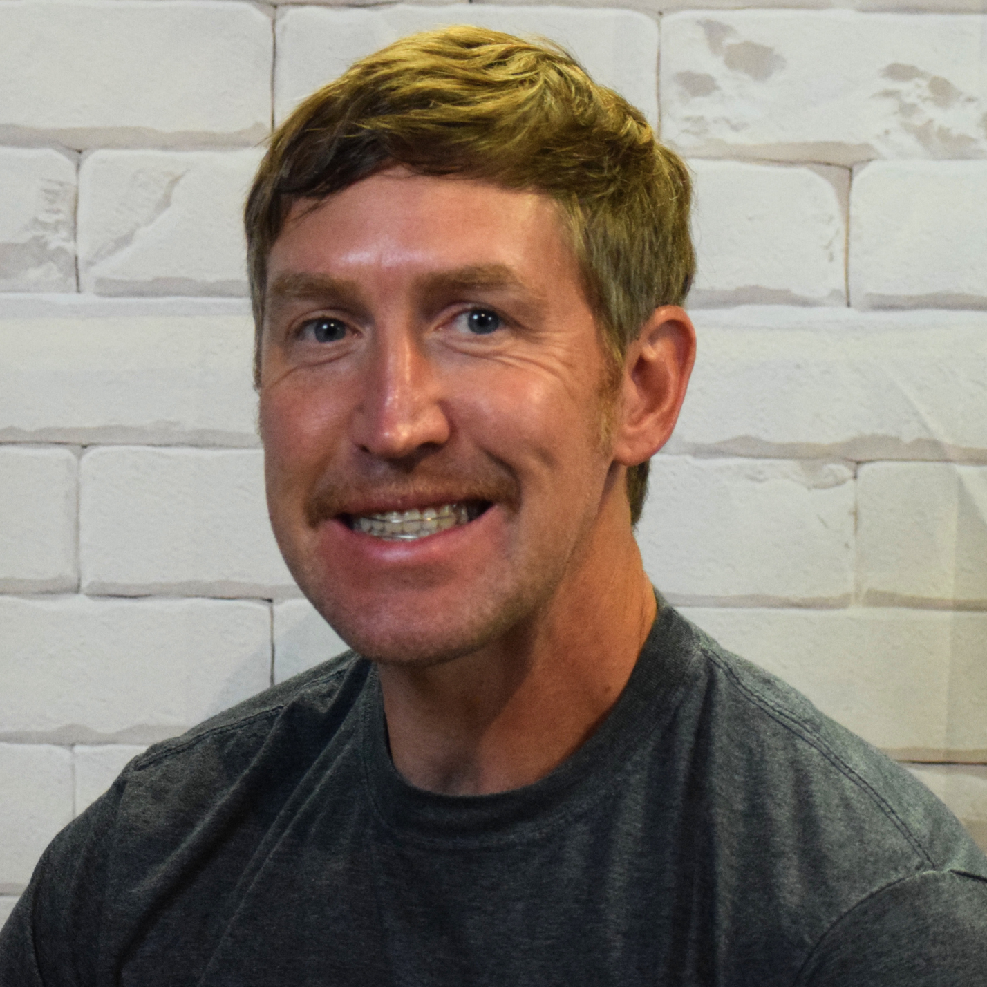 A bearded man wearing a grey shirt, looking thoughtfully into the distance.