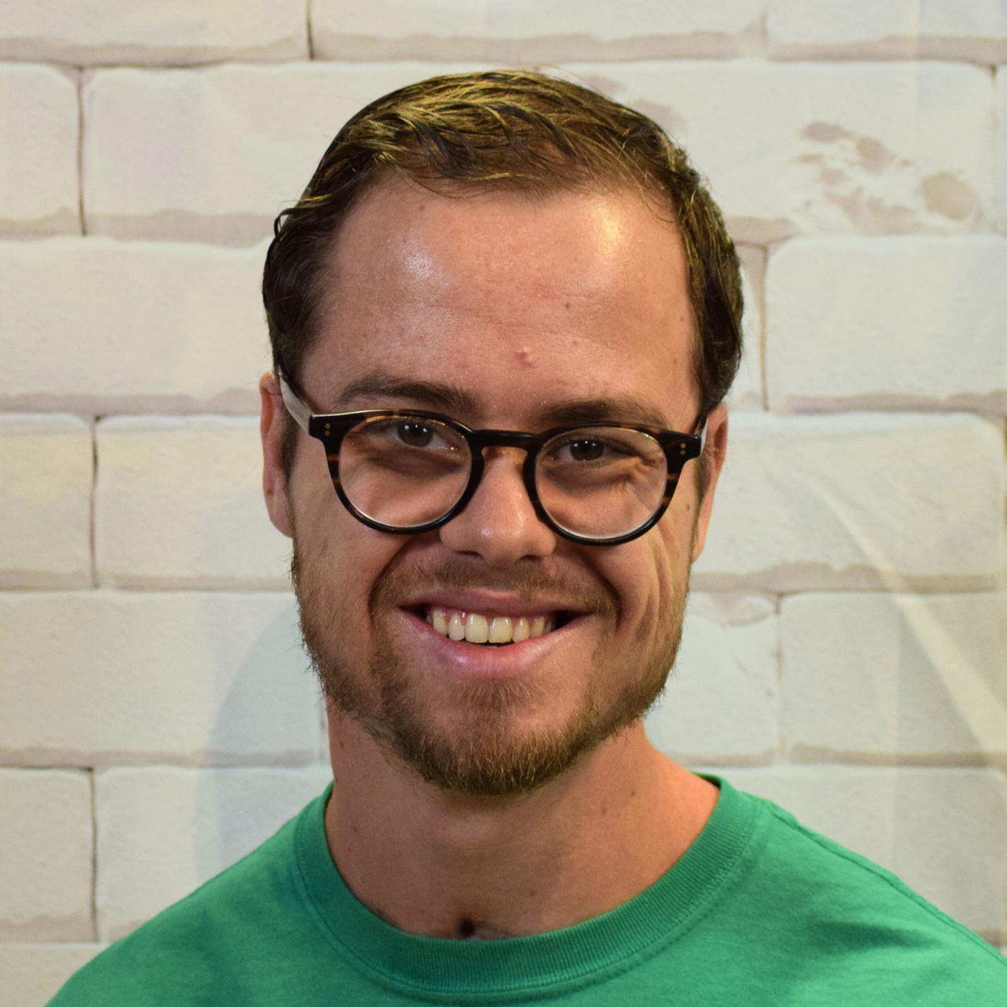 A smiling man wearing glasses and a gray shirt, exuding a friendly and approachable demeanor.