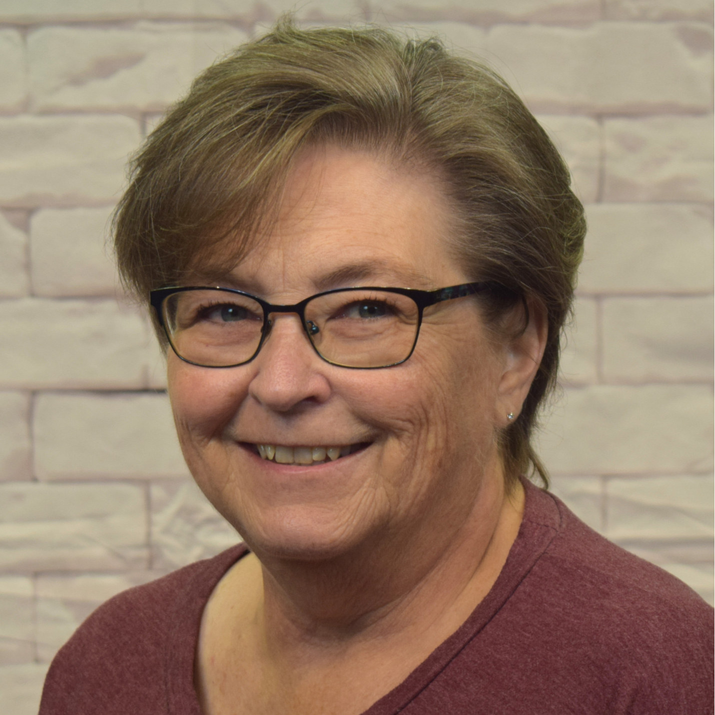 A woman wearing glasses and a red sweater smiles warmly, exuding a friendly and approachable demeanor.