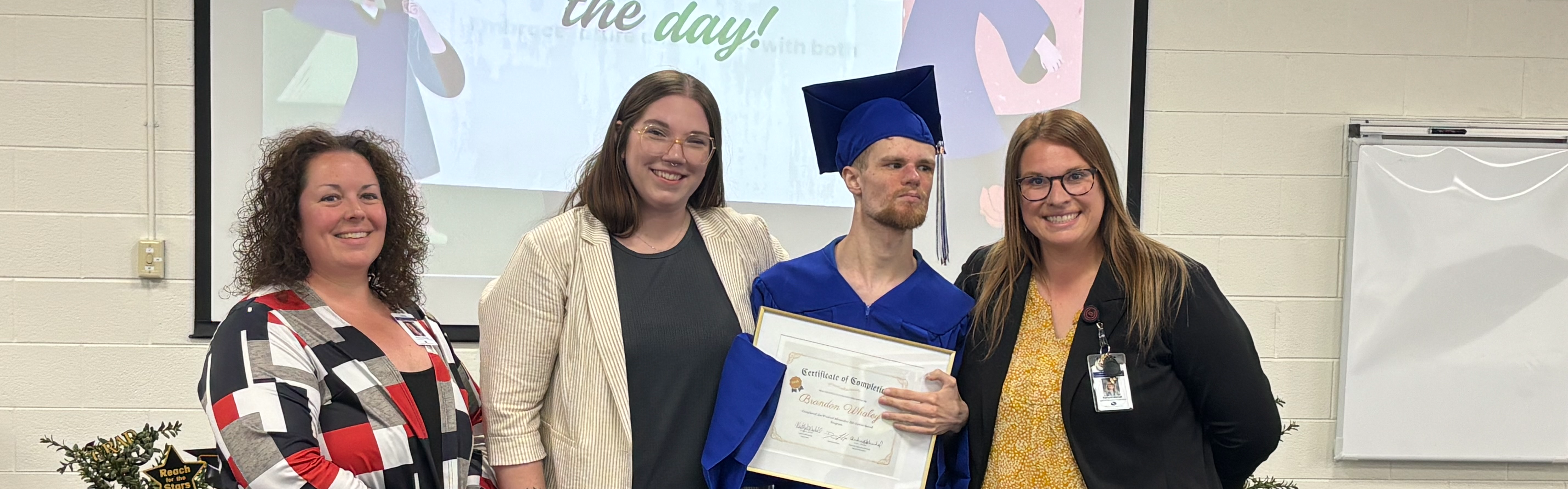 Student holding diploma standing next to staff