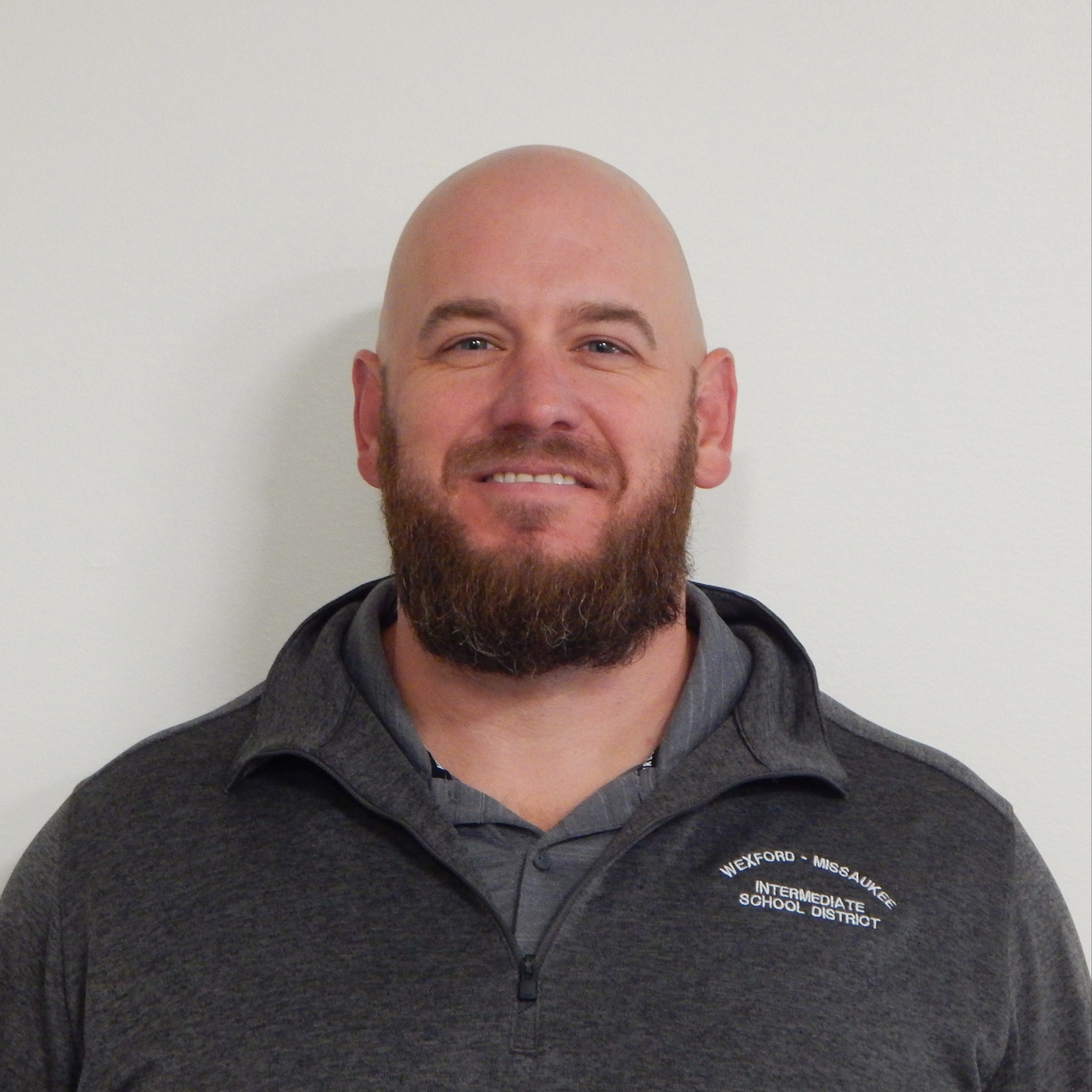 A man wearing a black shirt and a blue tie, standing confidently with a neutral expression.
