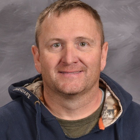 A man wearing a blue sweatshirt smiles warmly, exuding a friendly and approachable demeanor.