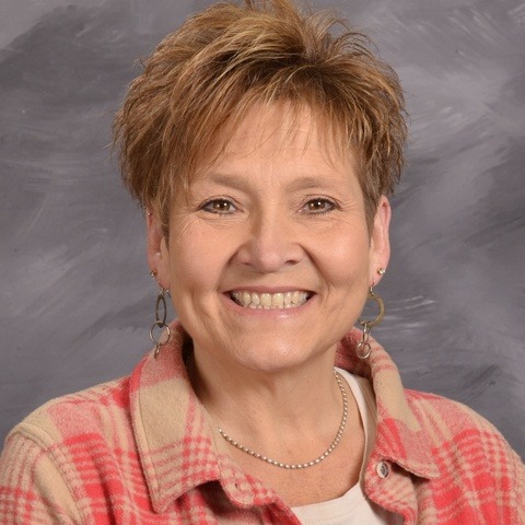 A woman wearing a white cardigan over a floral shirt, standing confidently with a pleasant expression.