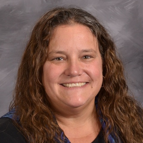 A woman wearing a blue and green shirt smiles warmly, radiating joy and positivity.