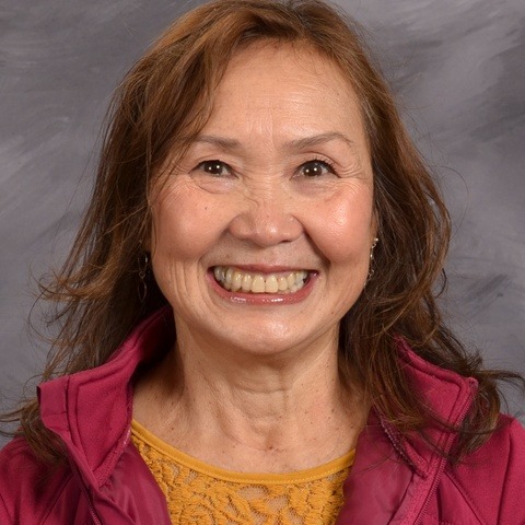 A woman wearing a pink shirt smiles brightly at the camera, exuding warmth and positivity.