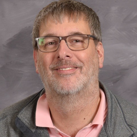 A smiling man wearing glasses and a blue shirt, exuding a friendly and approachable demeanor.
