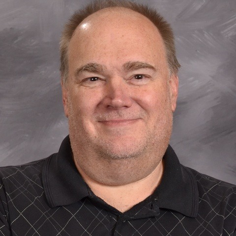 A man wearing a black shirt smiles warmly at the camera, exuding a friendly and approachable demeanor.