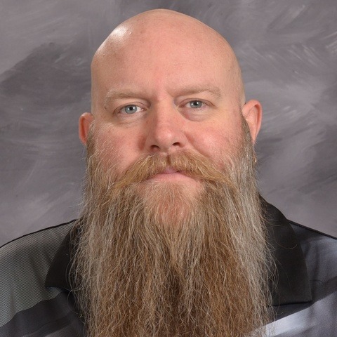 A man wearing a black shirt smiles warmly at the camera, exuding a friendly and approachable demeanor.