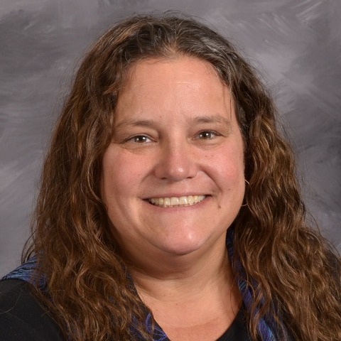 A woman wearing a blue and green shirt smiles warmly, radiating joy and positivity.