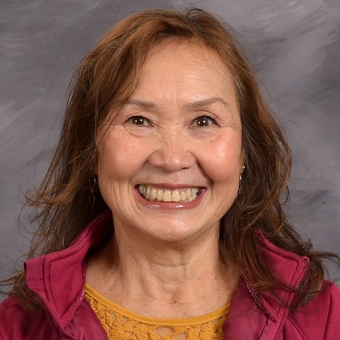 A woman wearing a pink shirt smiles brightly at the camera, exuding warmth and positivity.