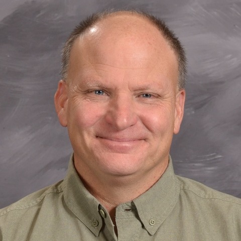 A man wearing a red and black shirt stands confidently against a neutral gray background.