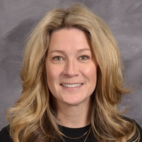 A woman wearing a cardigan sweater smiles warmly at the camera, exuding a friendly and inviting demeanor.