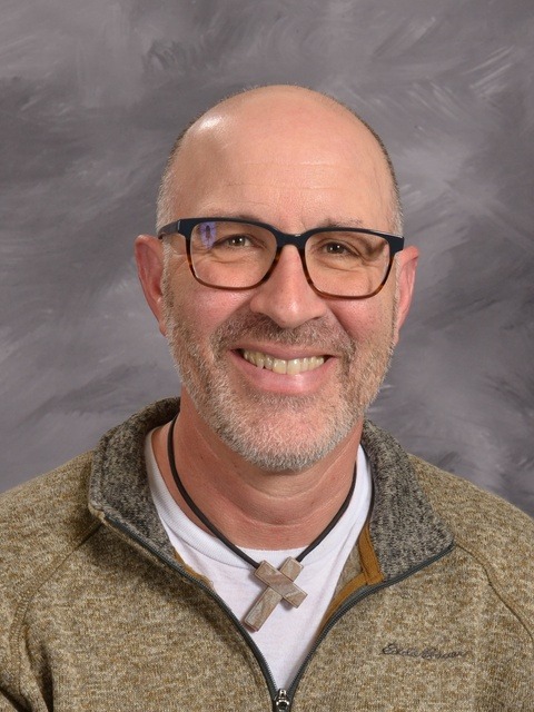 A smiling man wearing glasses and a green shirt, exuding a friendly and approachable demeanor.