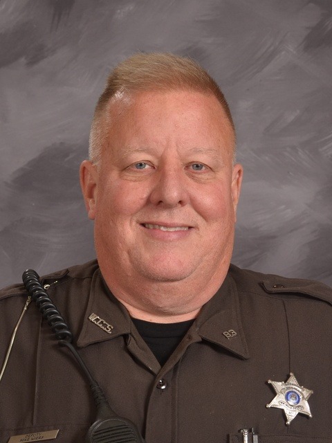 A police officer in uniform stands confidently in front of a closed door, ready for duty.