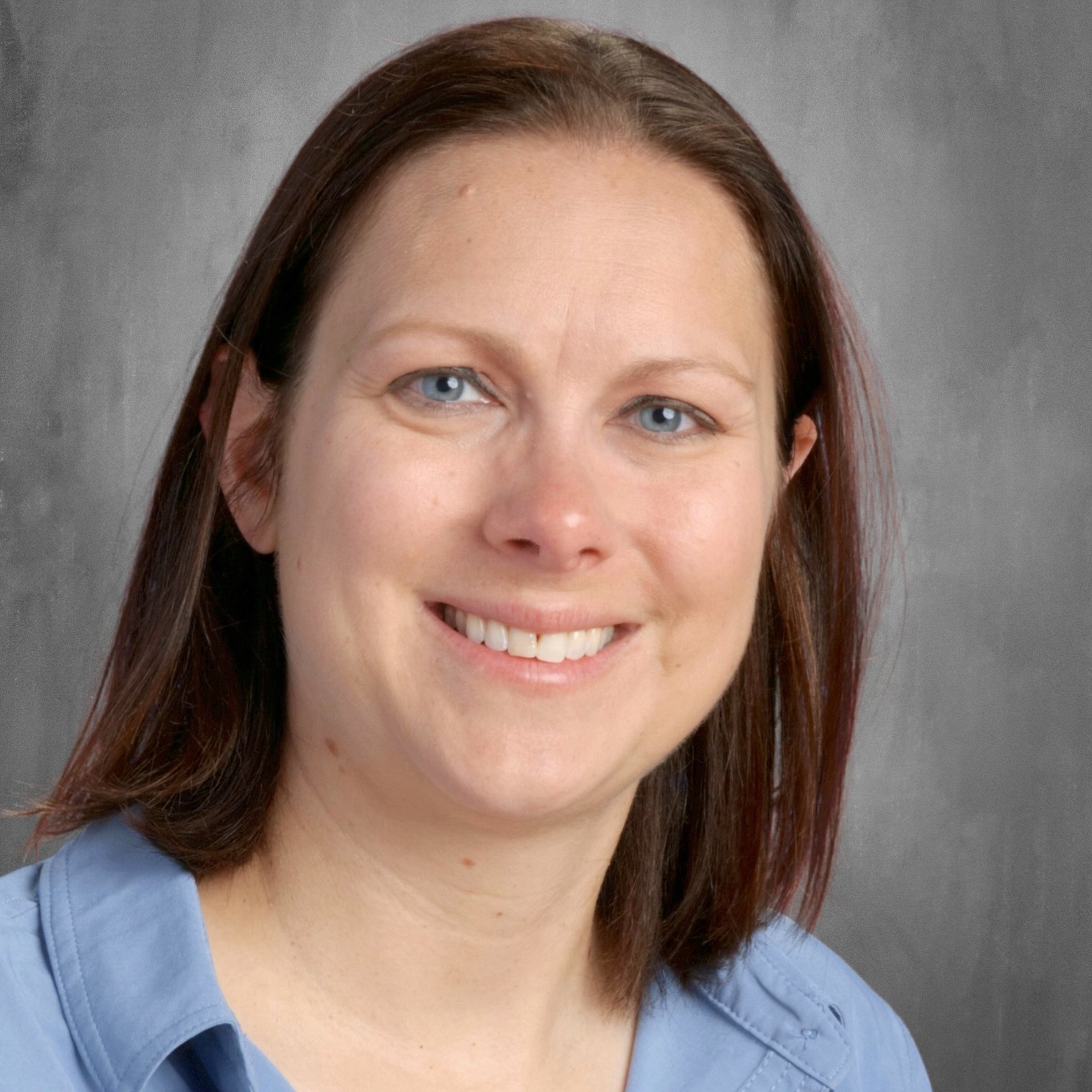 A woman with long hair wearing a blue shirt, standing confidently against a neutral background.