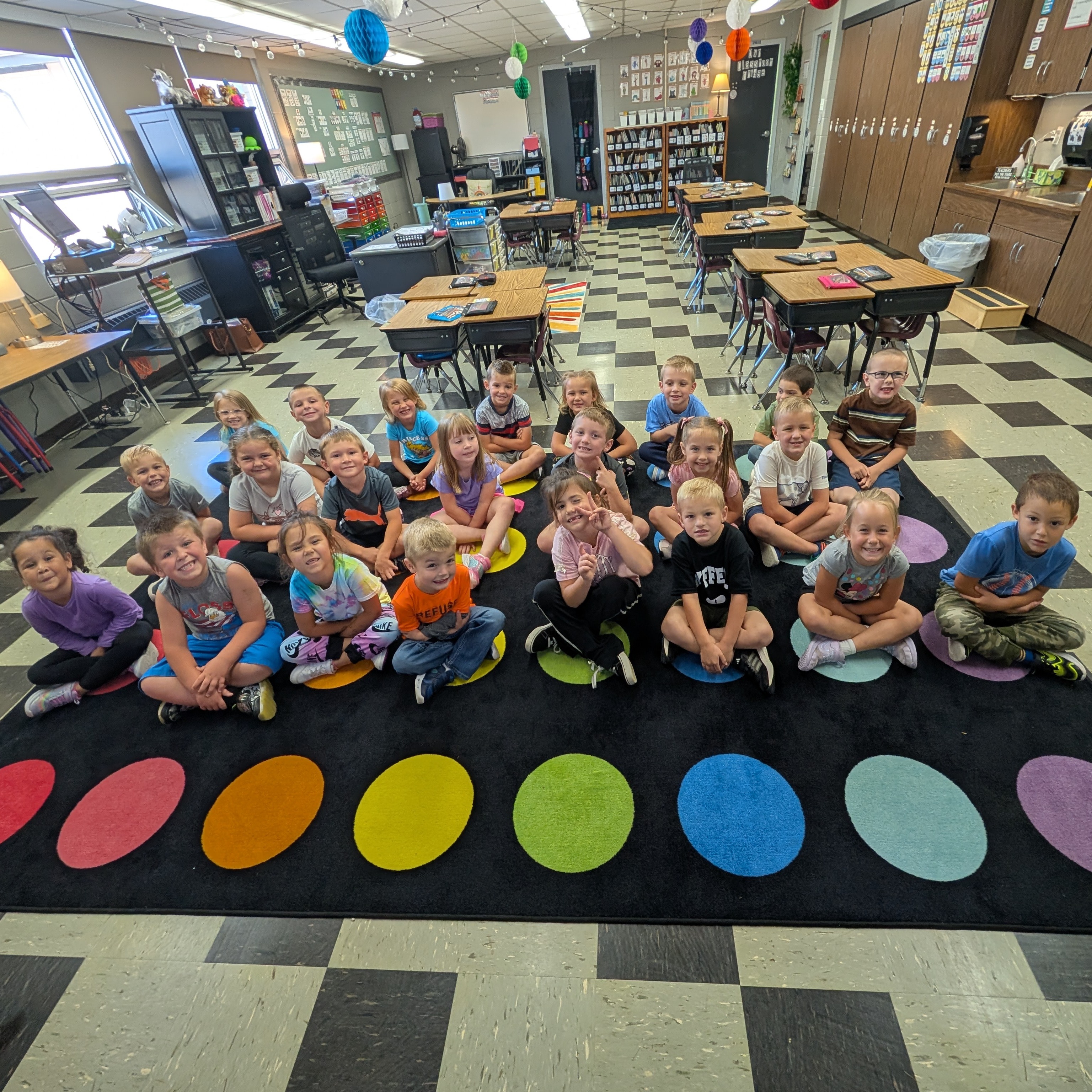 Kindergarten students are sitting on a  dot rug in the classroom.