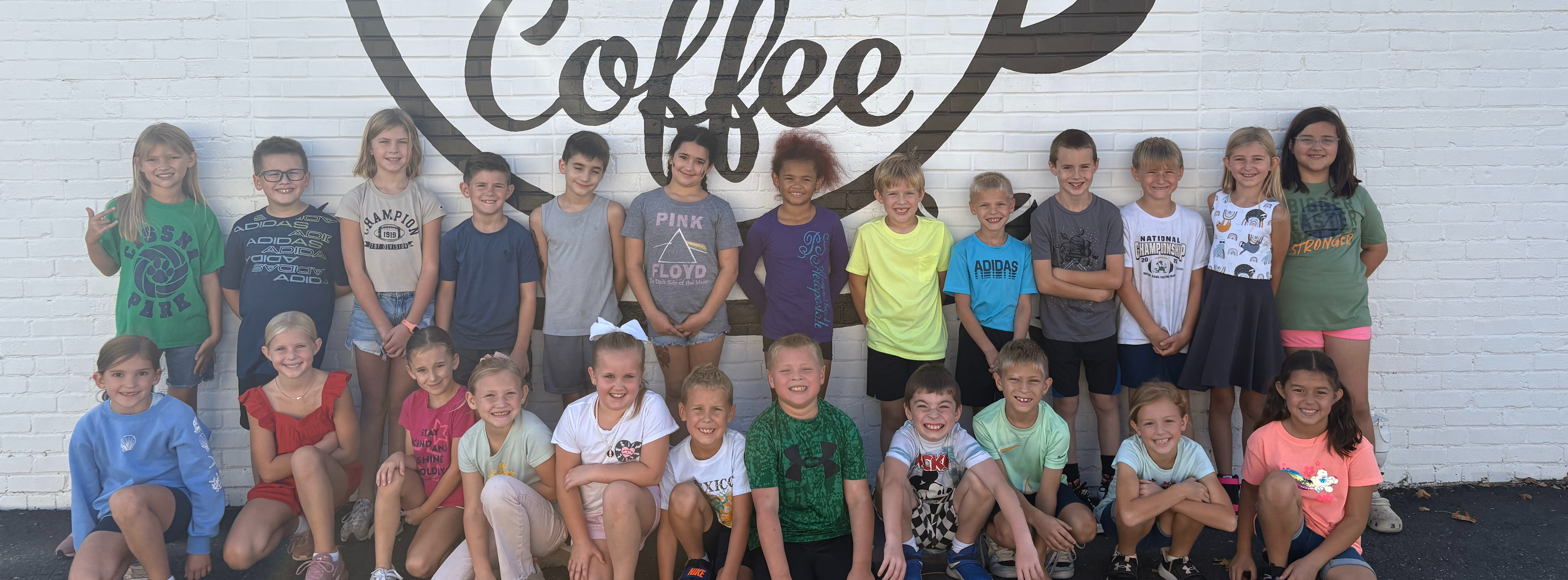 The third grade class is standing in front of the Kino's Coffee building.