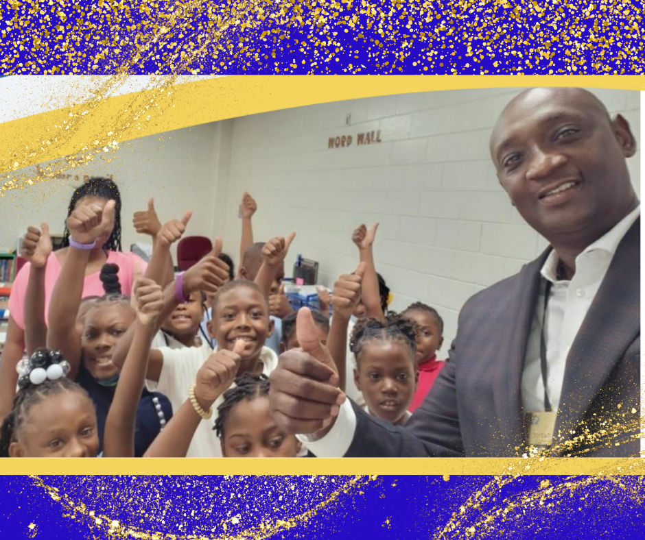 A man smiles and gives a thumbs up to children in a bright classroom, encouraging their learning and engagement.