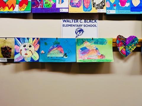 A display of colorful children's artwork hanging on a wall, featuring various drawings and a sign that reads 'WALTER C. BLACK ELEMENTARY SCHOOL.'