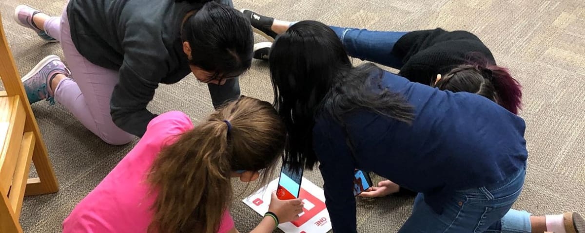 A group of four children are gathered on the floor, focused on a colorful educational activity or game laid out in front of them.