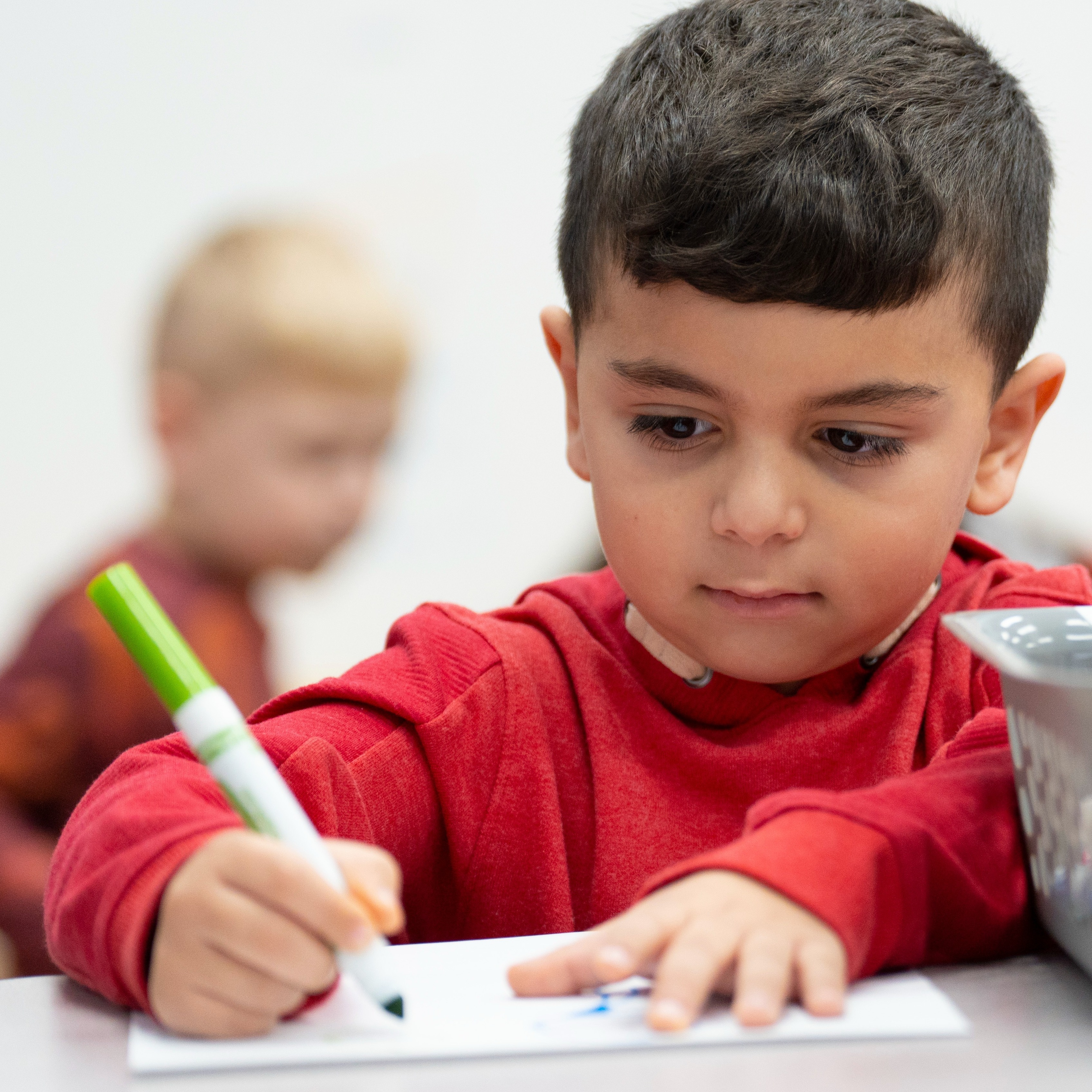 A preschooler writes on a piece of paper with a marker