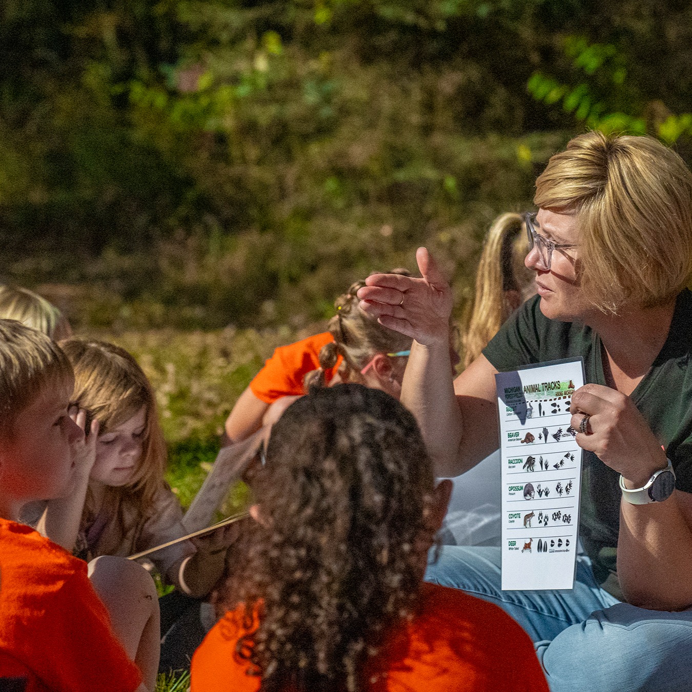 Pine River Nature Center naturalist holds up a sheet about identifying animal tracks to a group of elementary students during a field trip