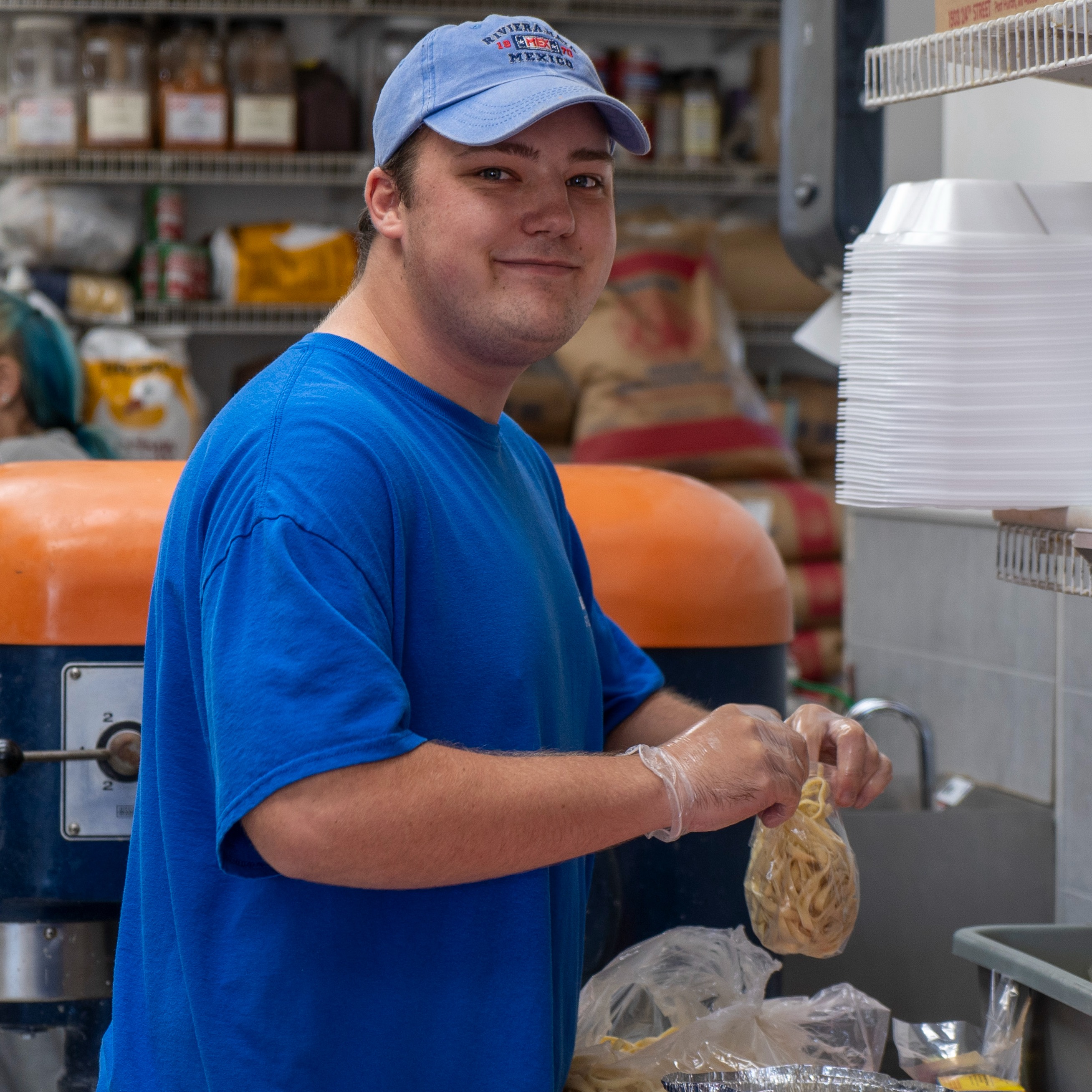A Next Step student wearing plastic gloves packages food in a commercial kitchen