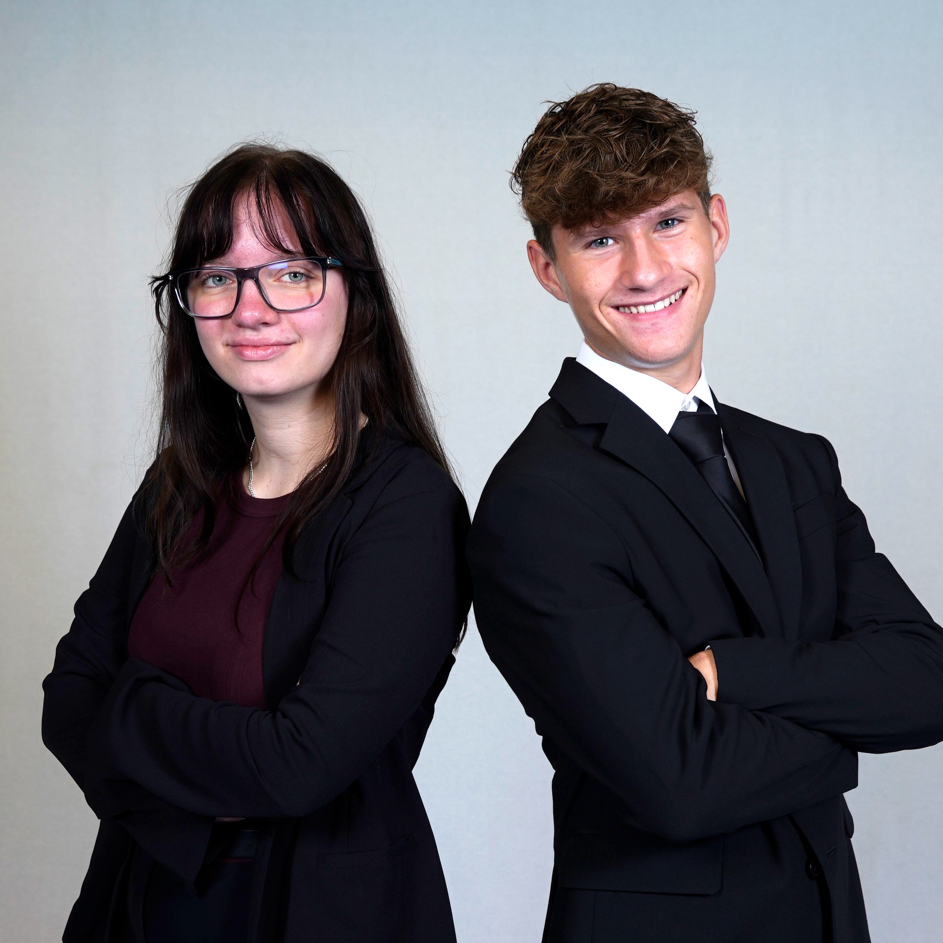 Two TEC students wearing professional business attire stand back to back with their arms crossed smiling at the camera
