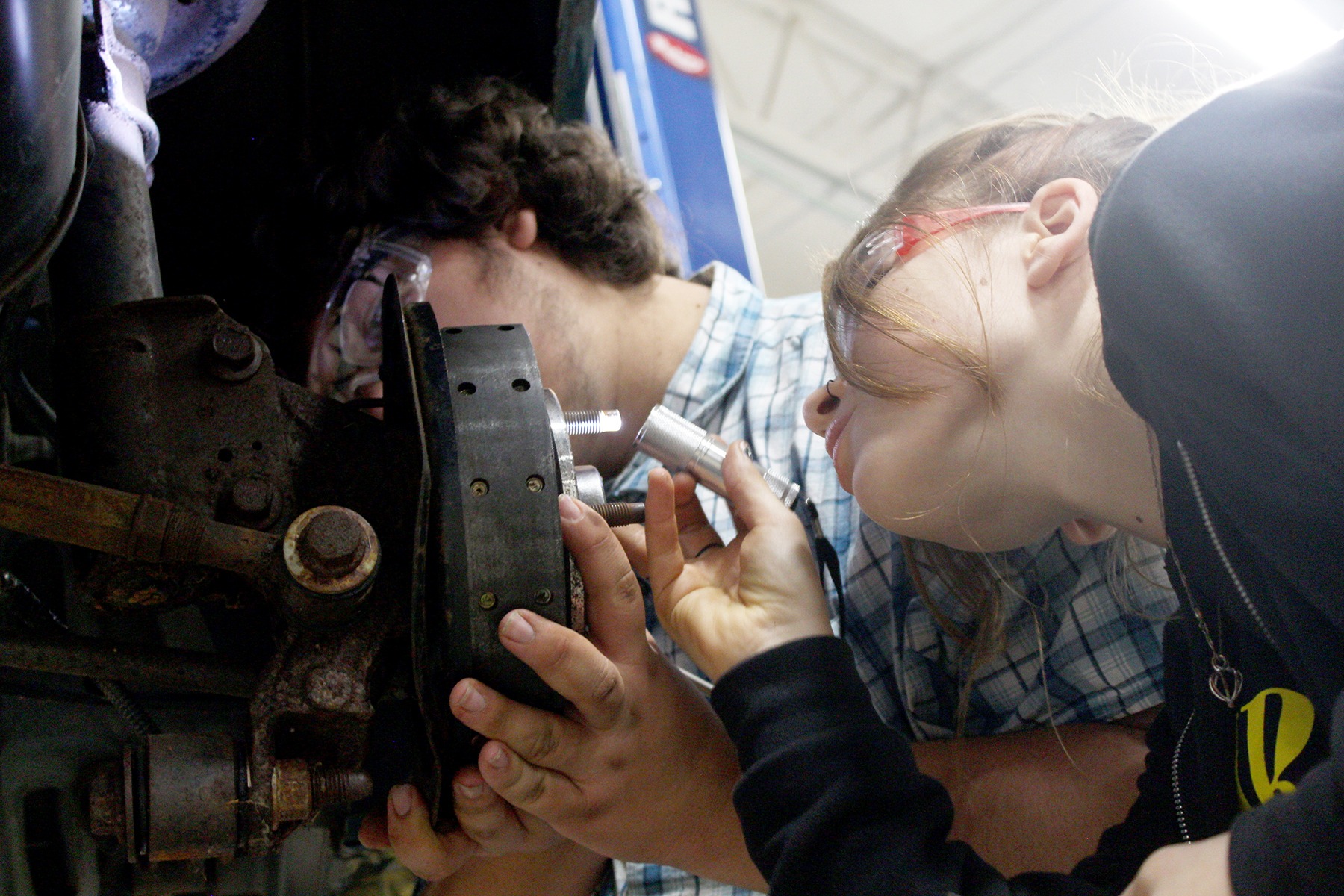 Two TEC students wearing safety glasses, work on the piece of machinery
