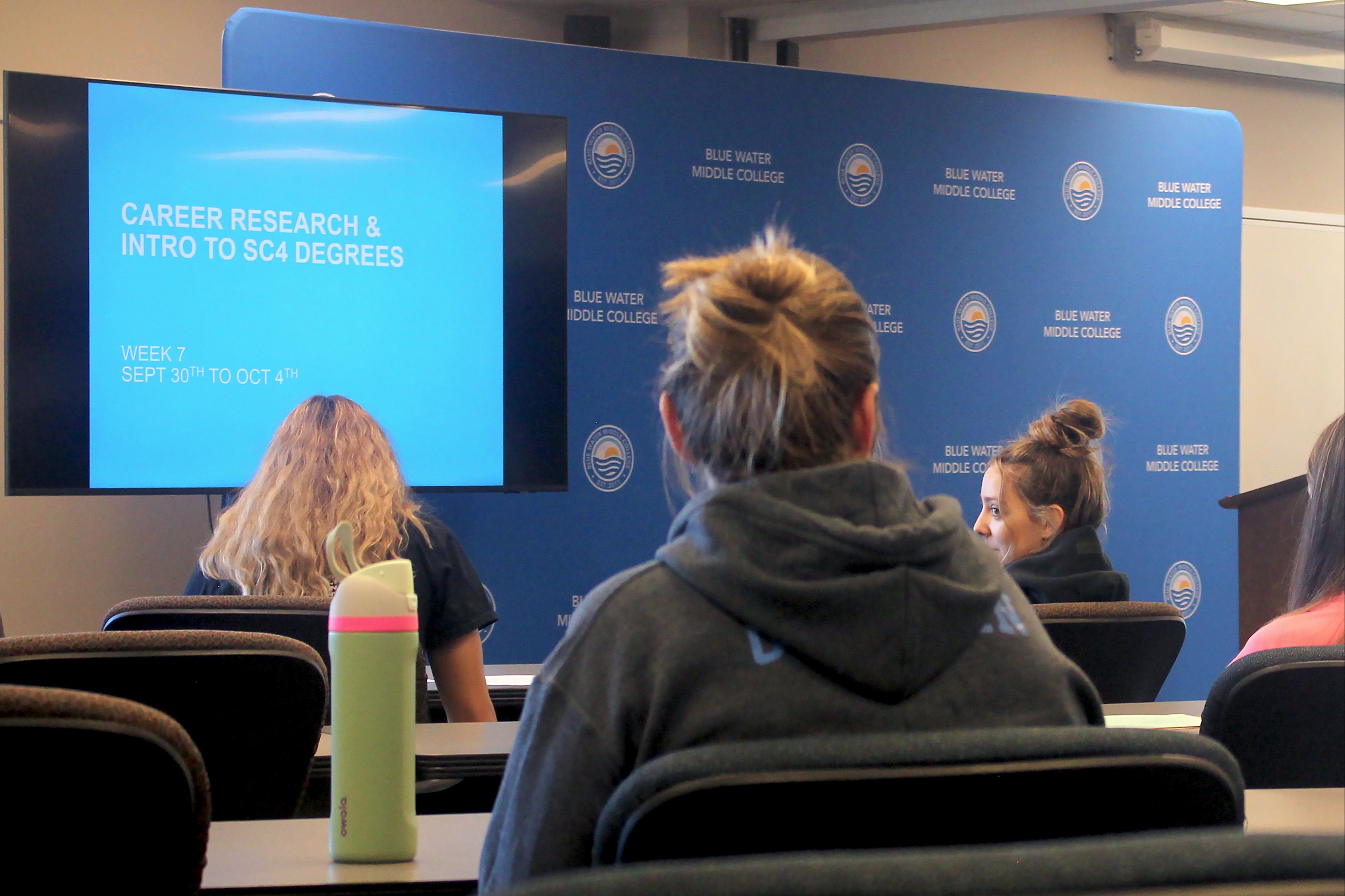 Students sit at tables with their backs to the camera, facing a screen as part of the BWMC seminar session