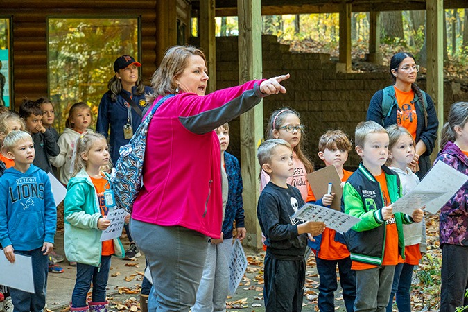 A nature center naturalist points in the distance as a group of elementary students look on