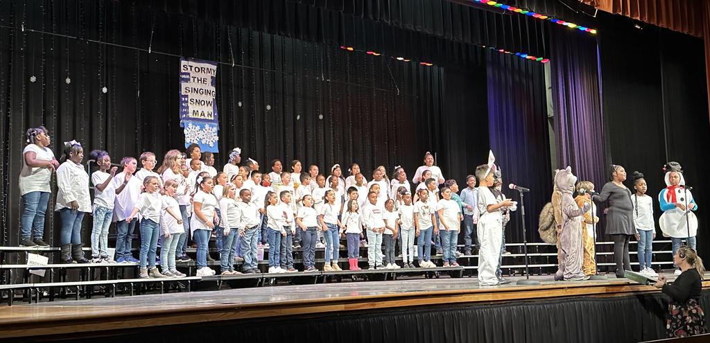 A school event featuring a choir and orchestra performing on stage, showcasing students' musical talents and teamwork.