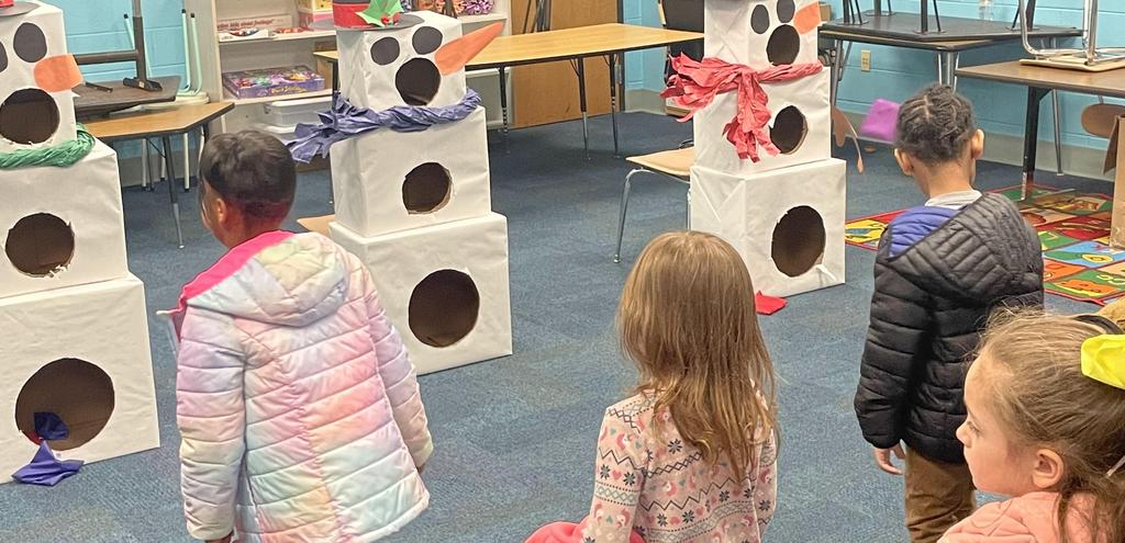 Children joyfully stand in a room surrounded by cheerful snowmen, creating a festive and playful atmosphere.