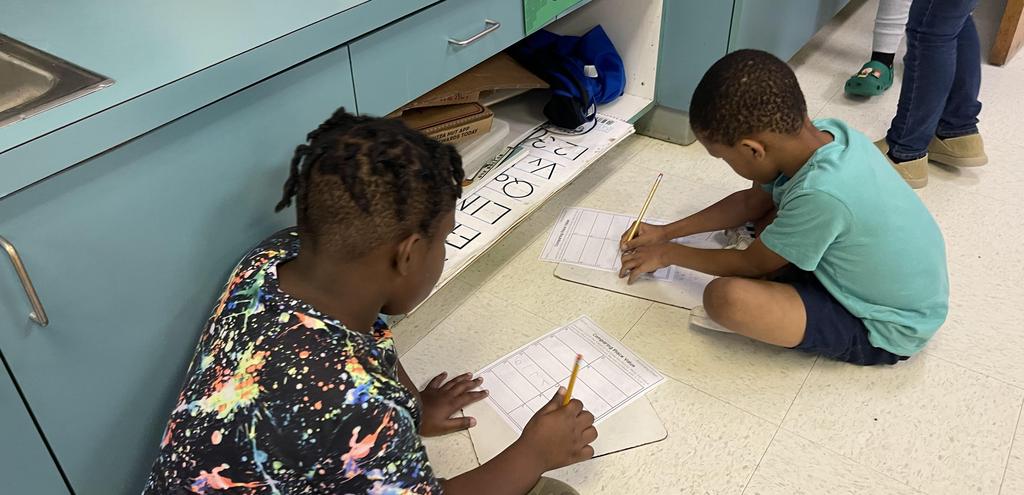 Two children seated on the floor, focused on writing on sheets of paper, showcasing creativity and concentration.
