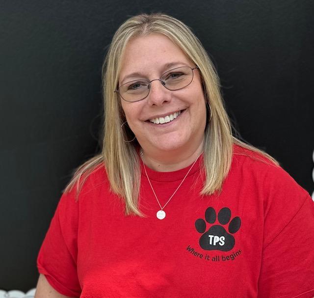 A woman wearing a red shirt smiles warmly, radiating joy and positivity in her expression.