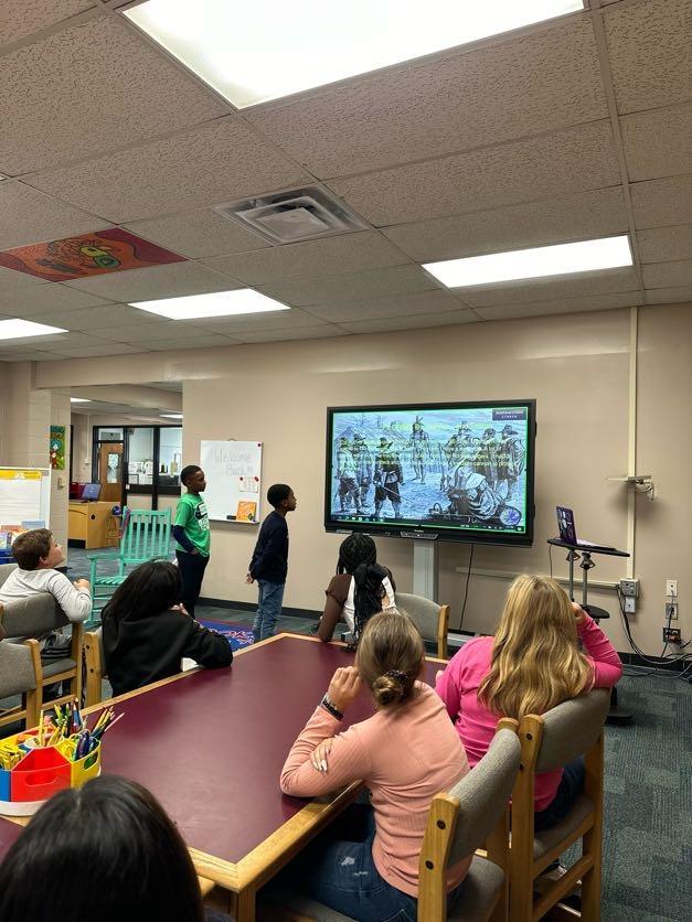 A group of children engaged in activities while sitting at tables in a bright classroom setting.