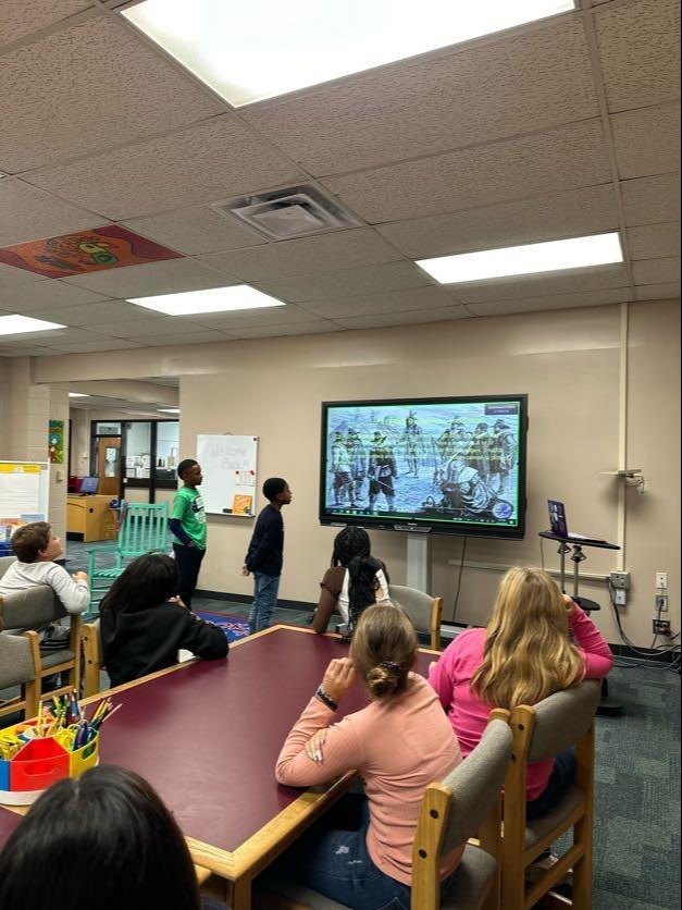 A group of children engaged in activities while sitting at tables in a bright classroom setting.