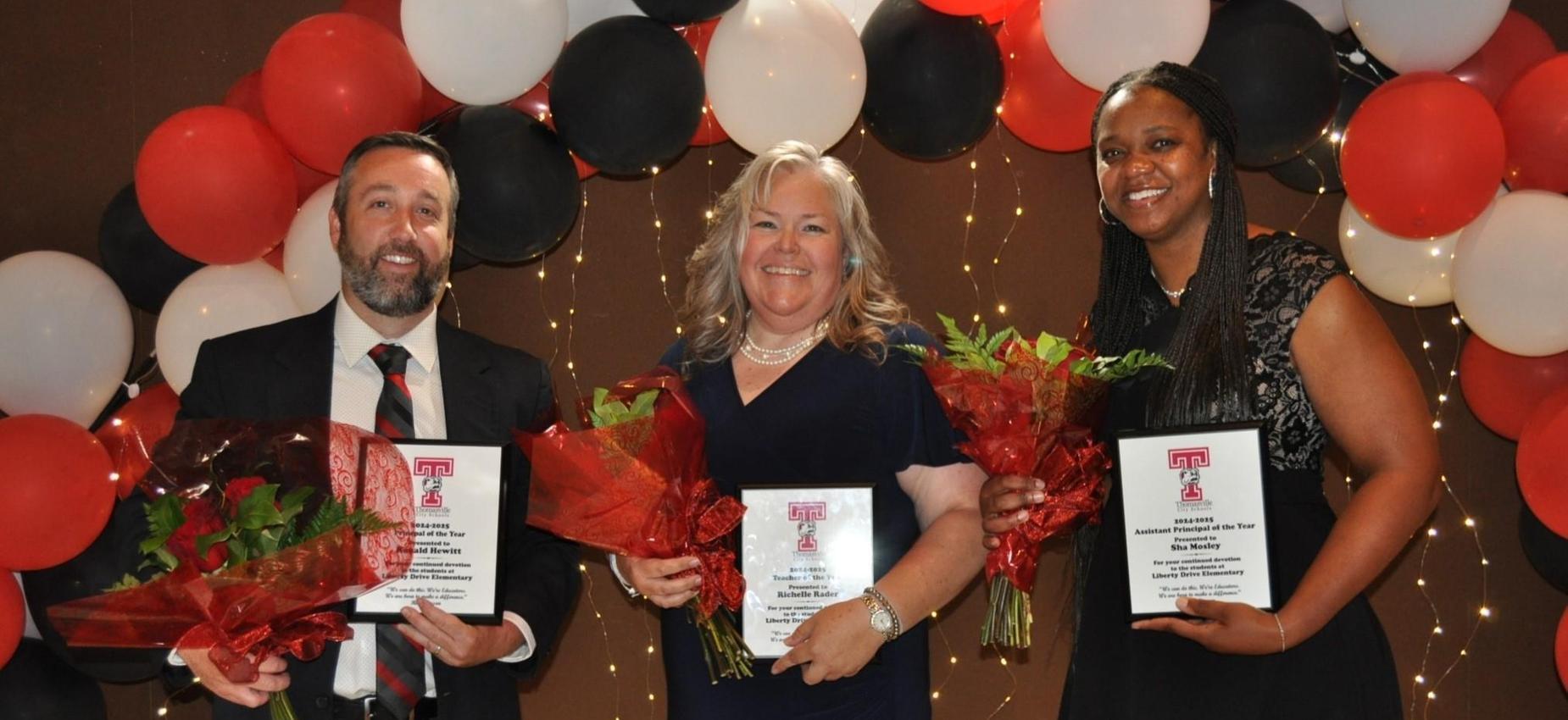 Three individuals proudly display their awards in front of colorful balloons, celebrating their achievements together.