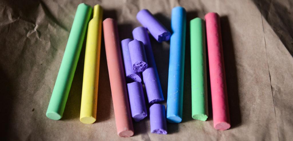 A vibrant assortment of chalk sticks in various colors arranged in a pile on a wooden table surface.