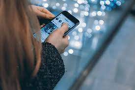 A woman is engaged with her phone while standing in front of a beautifully decorated Christmas tree.