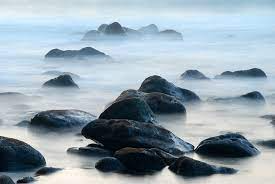 Rocks and ocean water illuminated by the soft hues of sunrise, creating a serene coastal landscape.